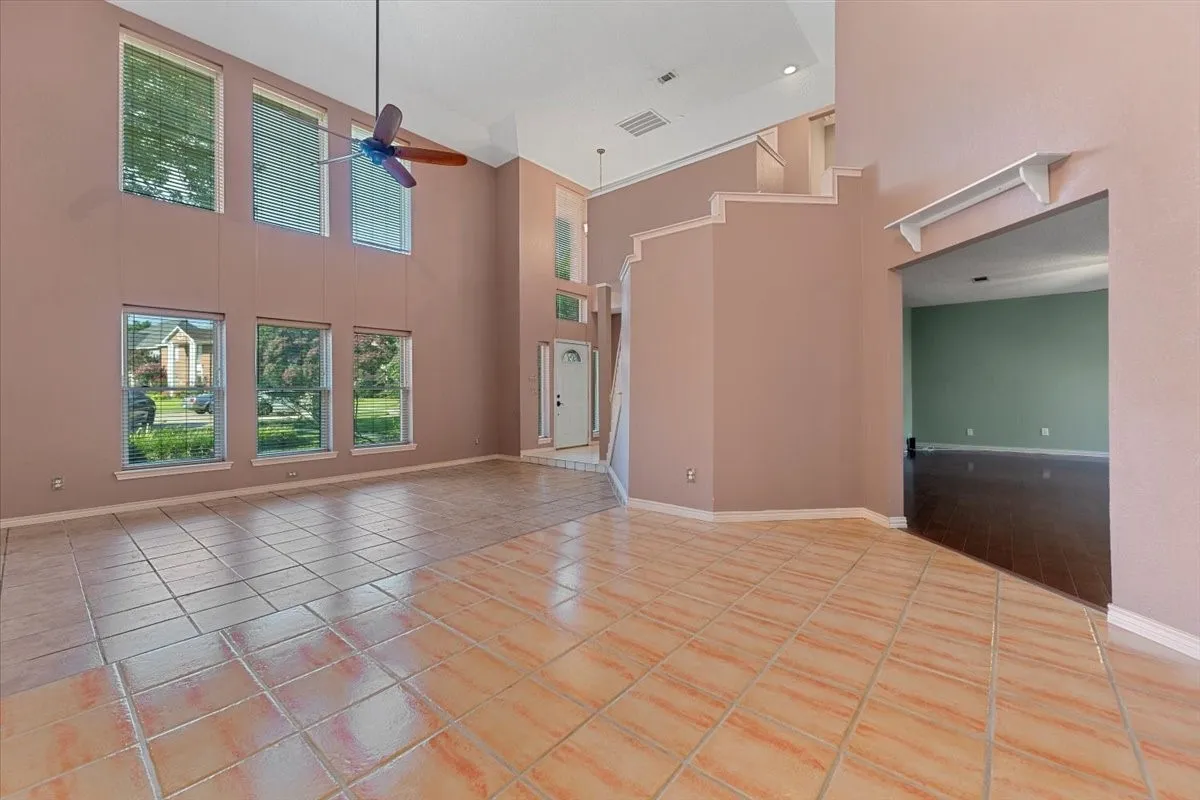 Unfurnished living room featuring light tile patterned flooring, a high ceiling, and ceiling fan