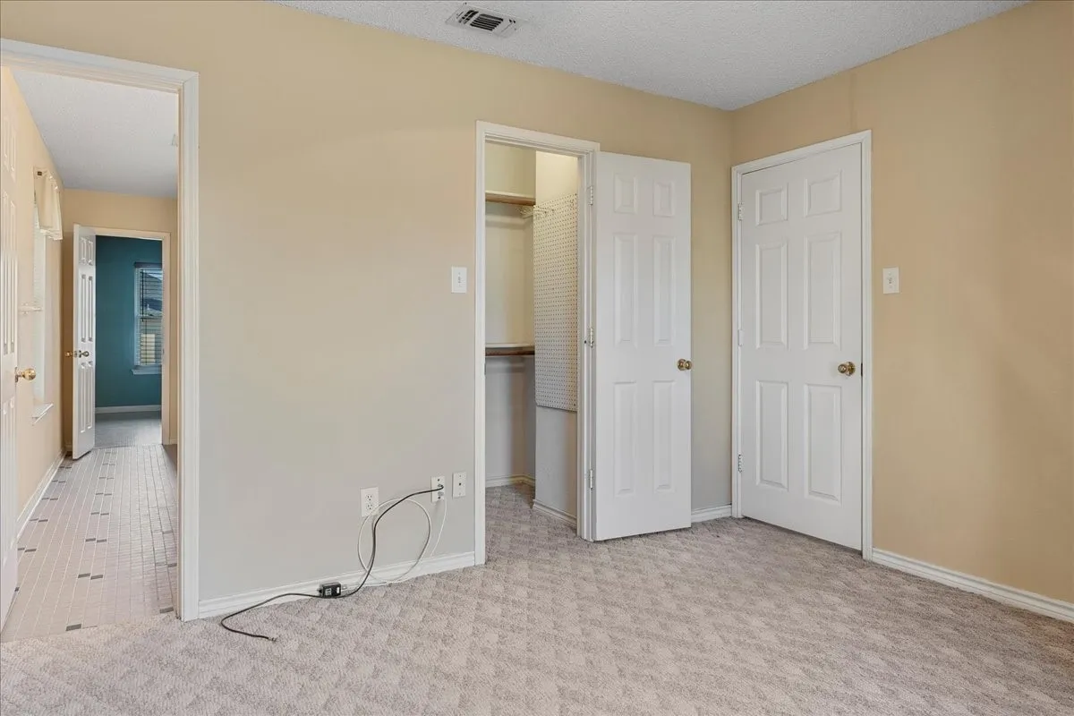 Unfurnished bedroom featuring a walk in closet, light carpet, and a textured ceiling