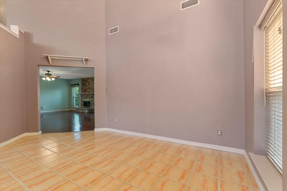 Spare room featuring a towering ceiling, ceiling fan, plenty of natural light, a fireplace, and light tile patterned floors