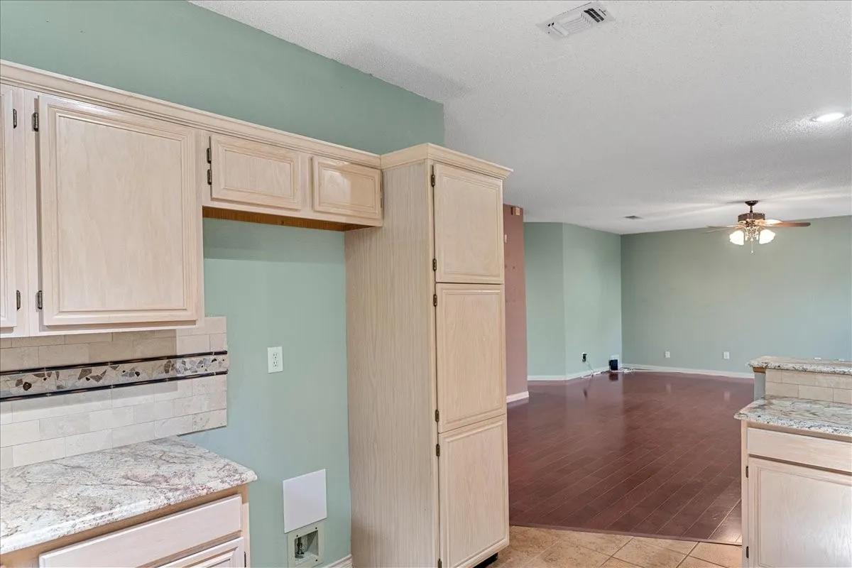 Kitchen featuring light brown cabinets, decorative backsplash, a ceiling fan, open floor plan, and light tile patterned floors