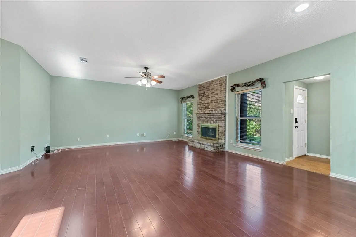 Unfurnished living room with wood-type flooring, a brick fireplace, and ceiling fan