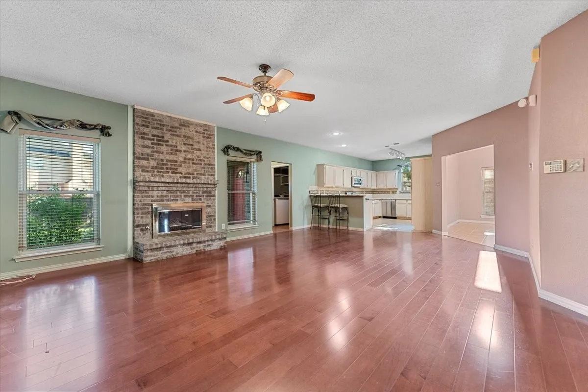 Unfurnished living room with a fireplace, dark wood-type flooring, a textured ceiling, and a ceiling fan