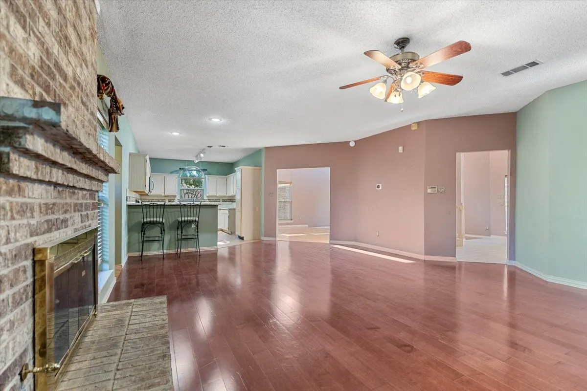 Unfurnished living room with a fireplace, dark wood-style flooring, a textured ceiling, and ceiling fan