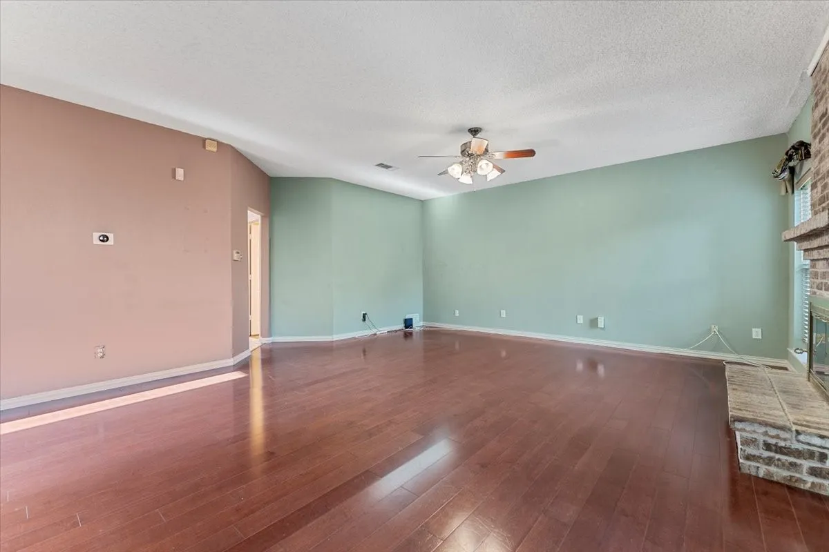 Unfurnished living room with dark wood finished floors, ceiling fan, a brick fireplace, and a textured ceiling