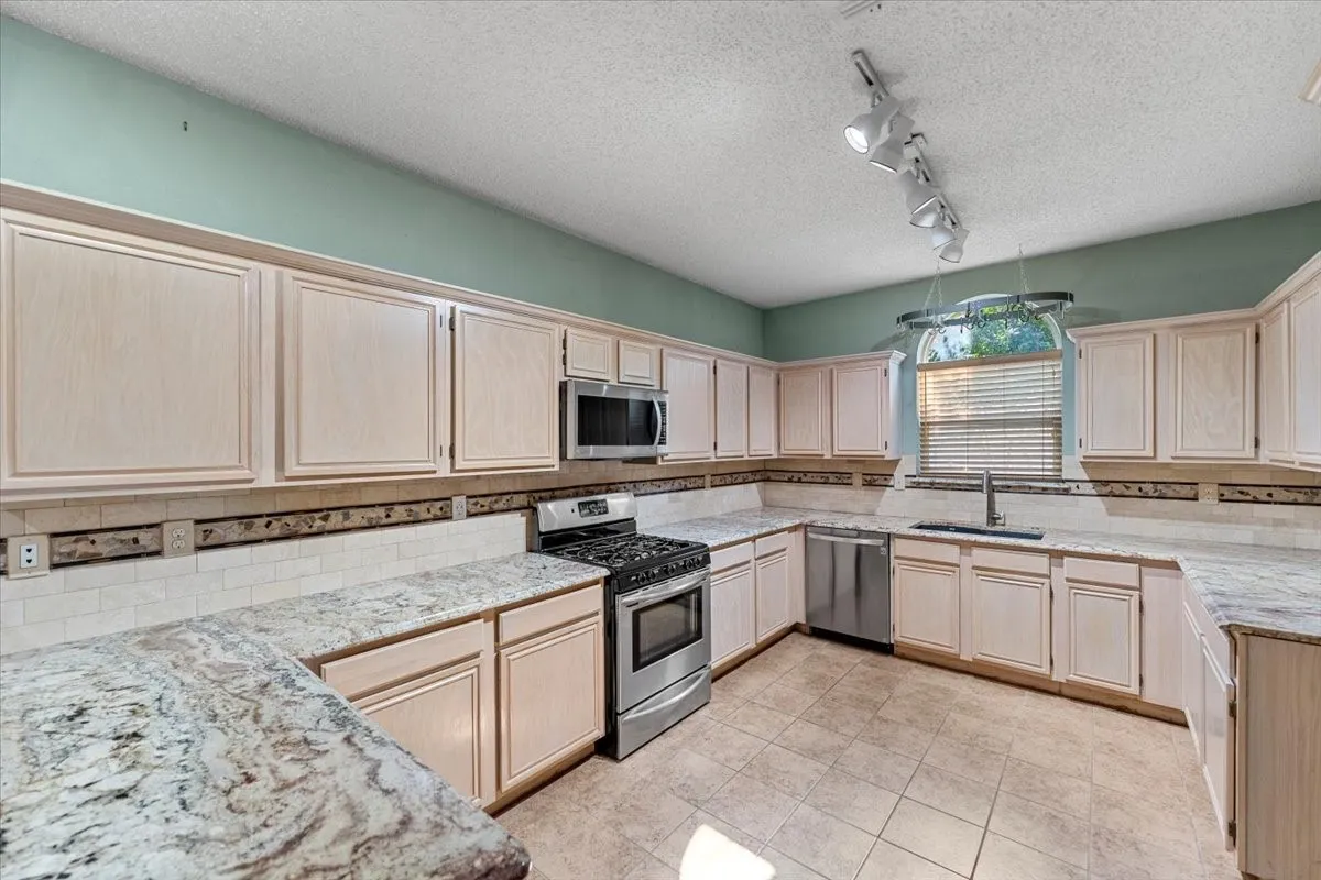Kitchen featuring light brown cabinets, decorative backsplash, stainless steel appliances, a textured ceiling, and rail lighting