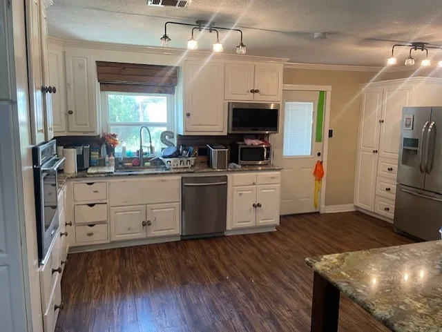 Kitchen with dark stone countertops, stainless steel appliances, a textured ceiling, ornamental molding, and track lighting