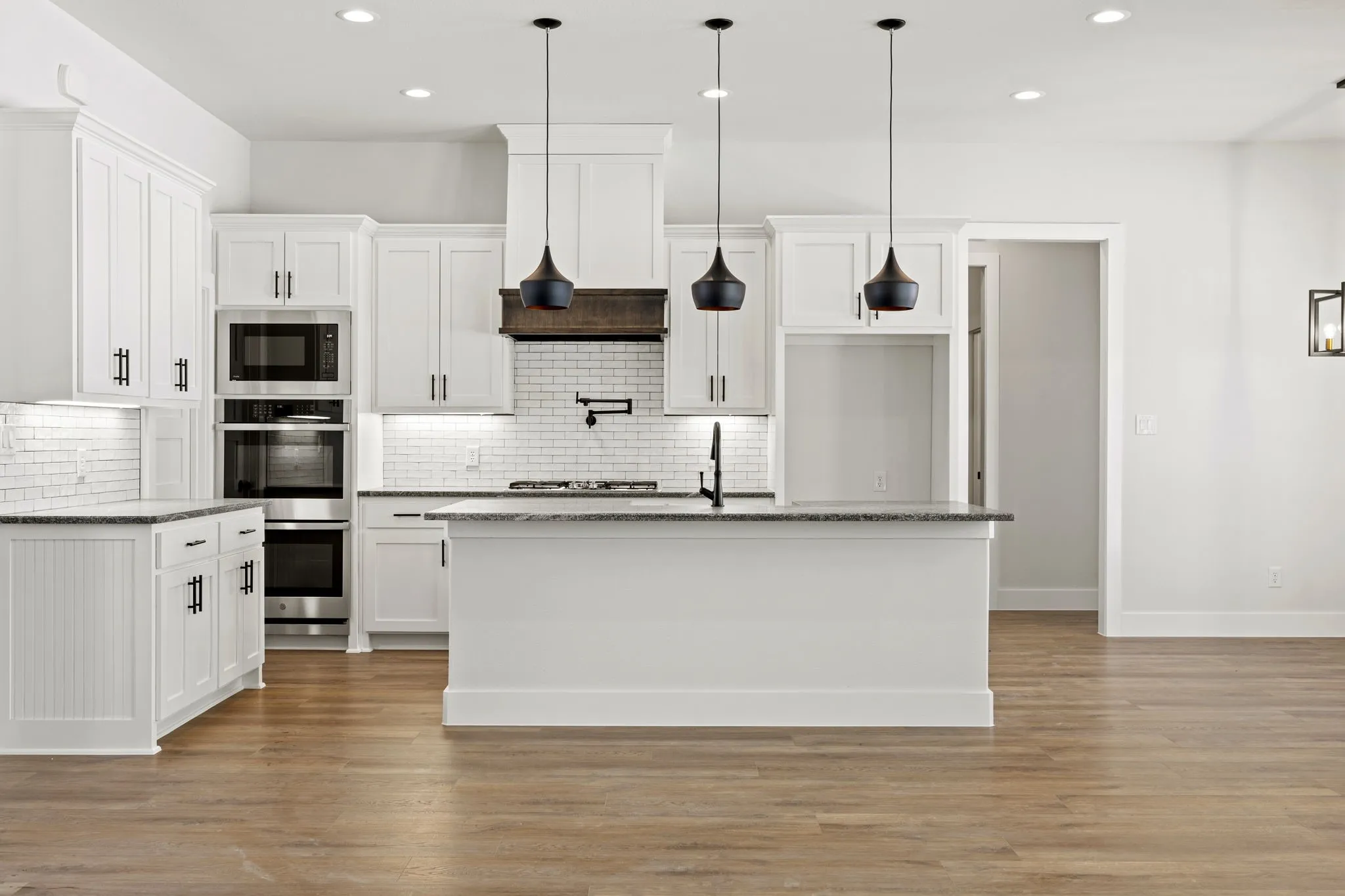 Kitchen with light stone countertops, white cabinets, an island with sink, and light wood finished floors