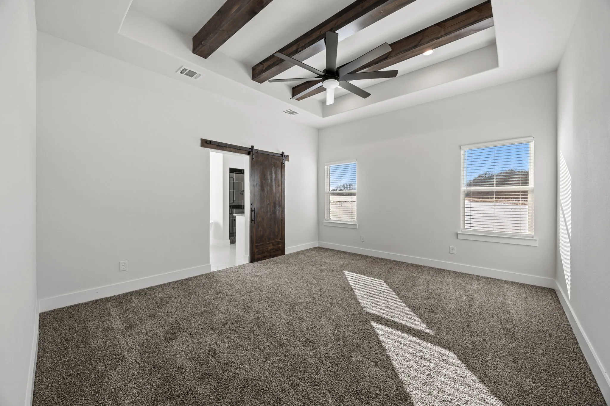 Unfurnished bedroom with a barn door, beamed ceiling, carpet, ceiling fan, and a tray ceiling