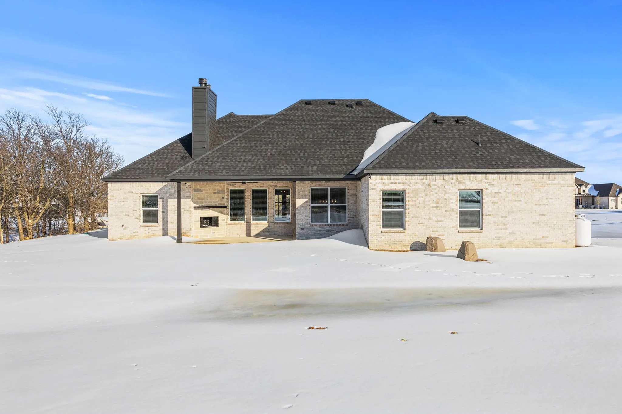 Snow covered house with a patio, brick siding, and a chimney