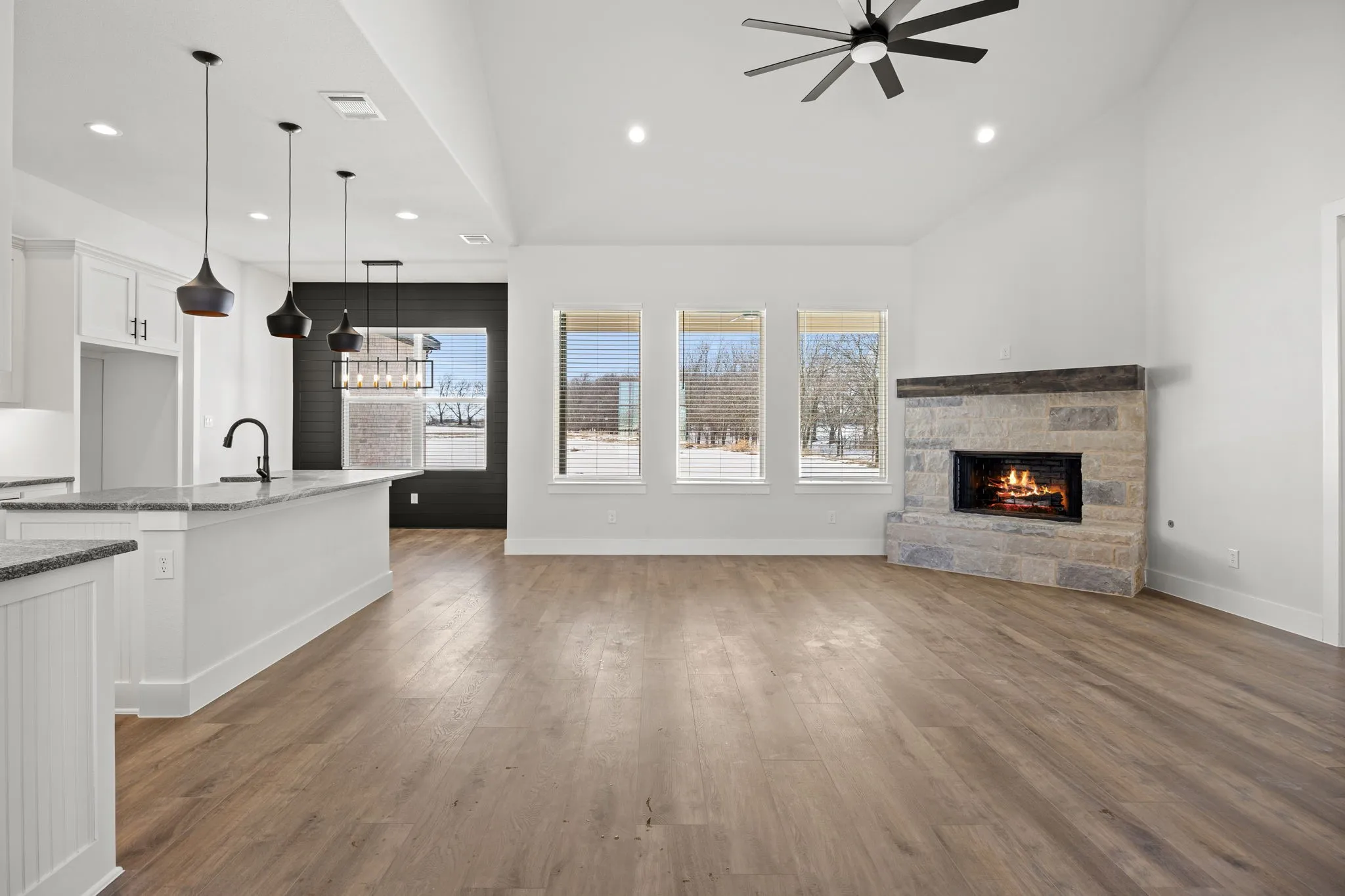 Unfurnished living room featuring a stone fireplace, dark wood-style floors, a high ceiling, a ceiling fan, and recessed lighting