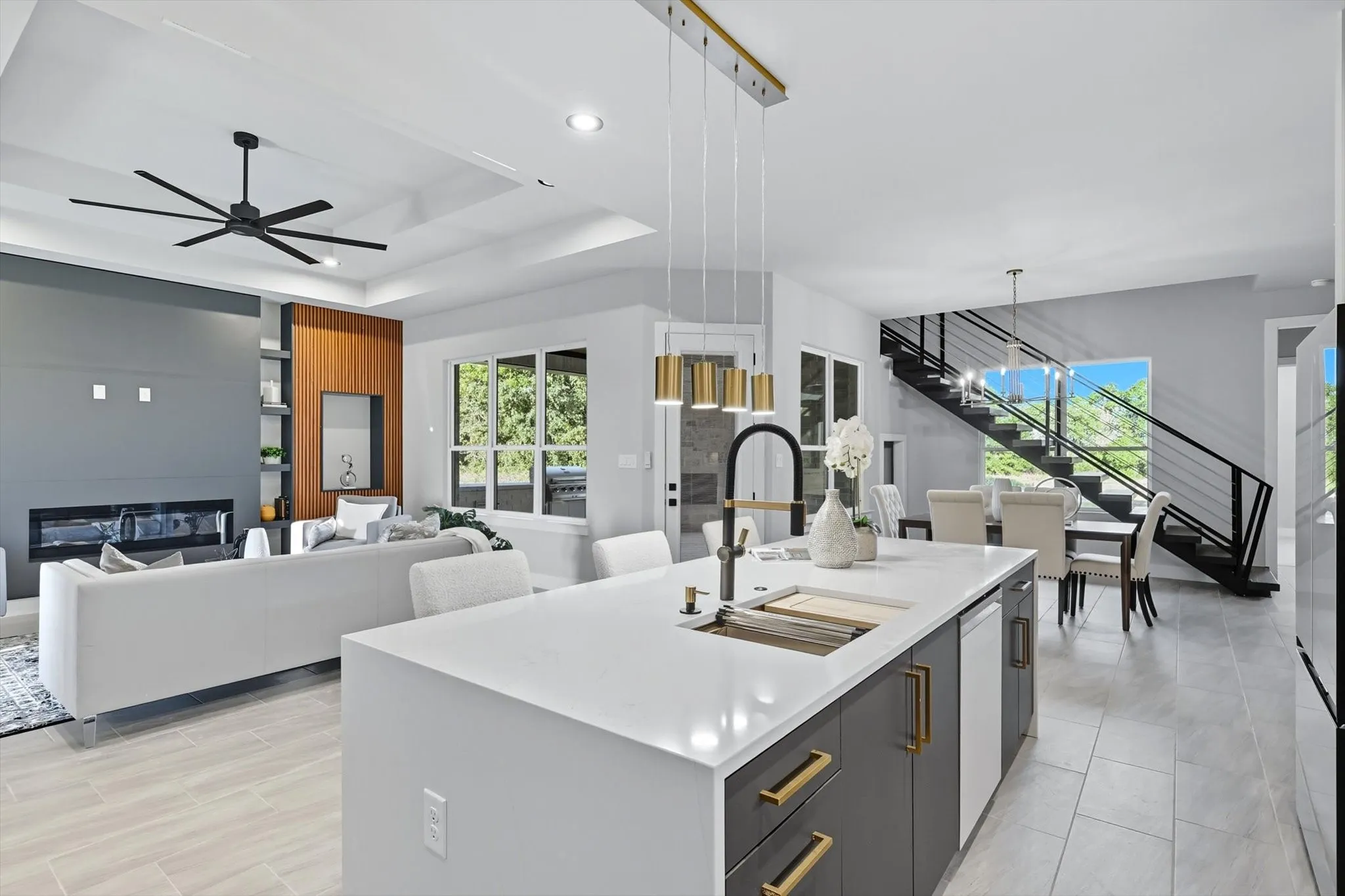 Kitchen with a glass covered fireplace, a tray ceiling, an island with sink, hanging light fixtures, and modern cabinets