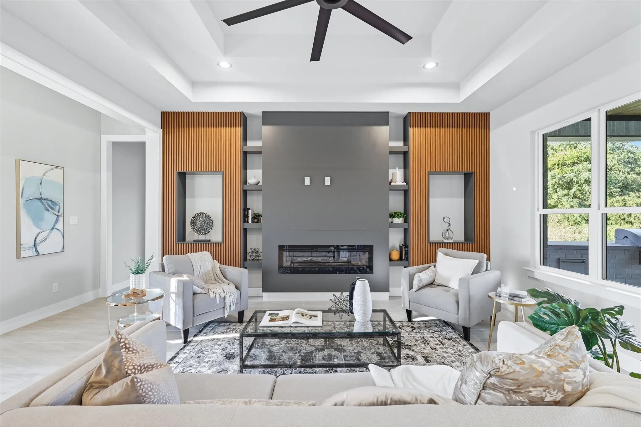 Living room with a glass covered fireplace, a raised ceiling, recessed lighting, a ceiling fan, and built in shelves