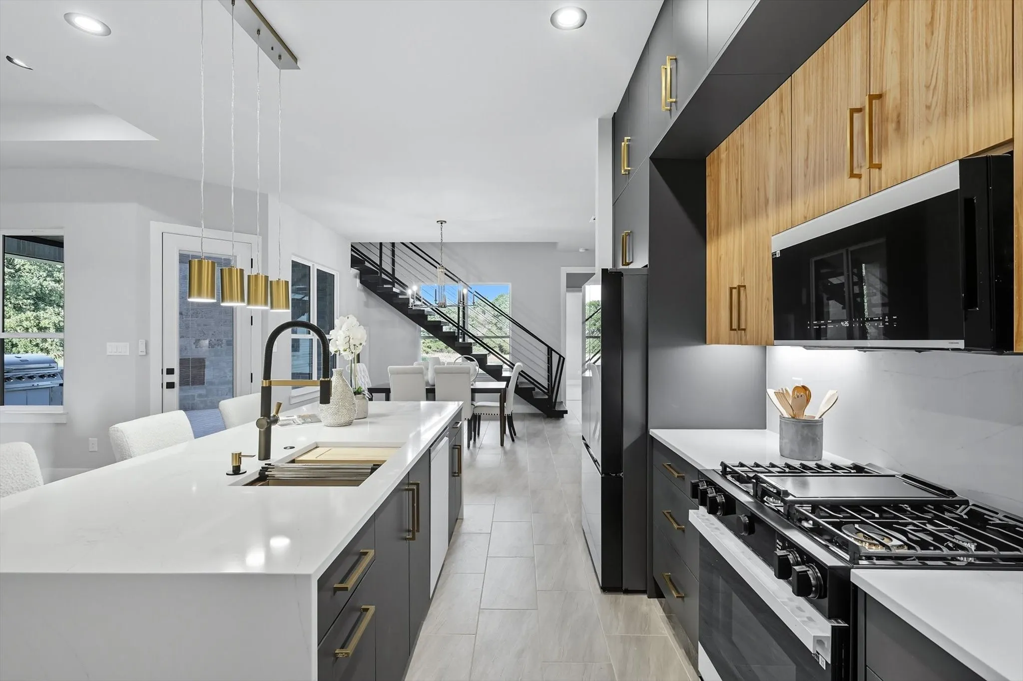 Kitchen with black appliances, modern cabinets, decorative light fixtures, light stone counters, and a breakfast bar