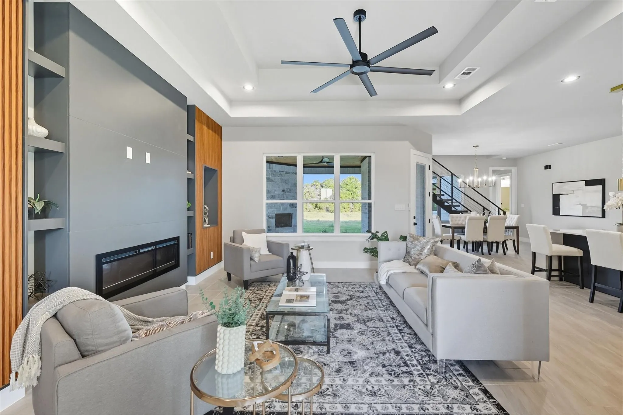 Living room with a tray ceiling, a large fireplace, a chandelier, recessed lighting, and a ceiling fan