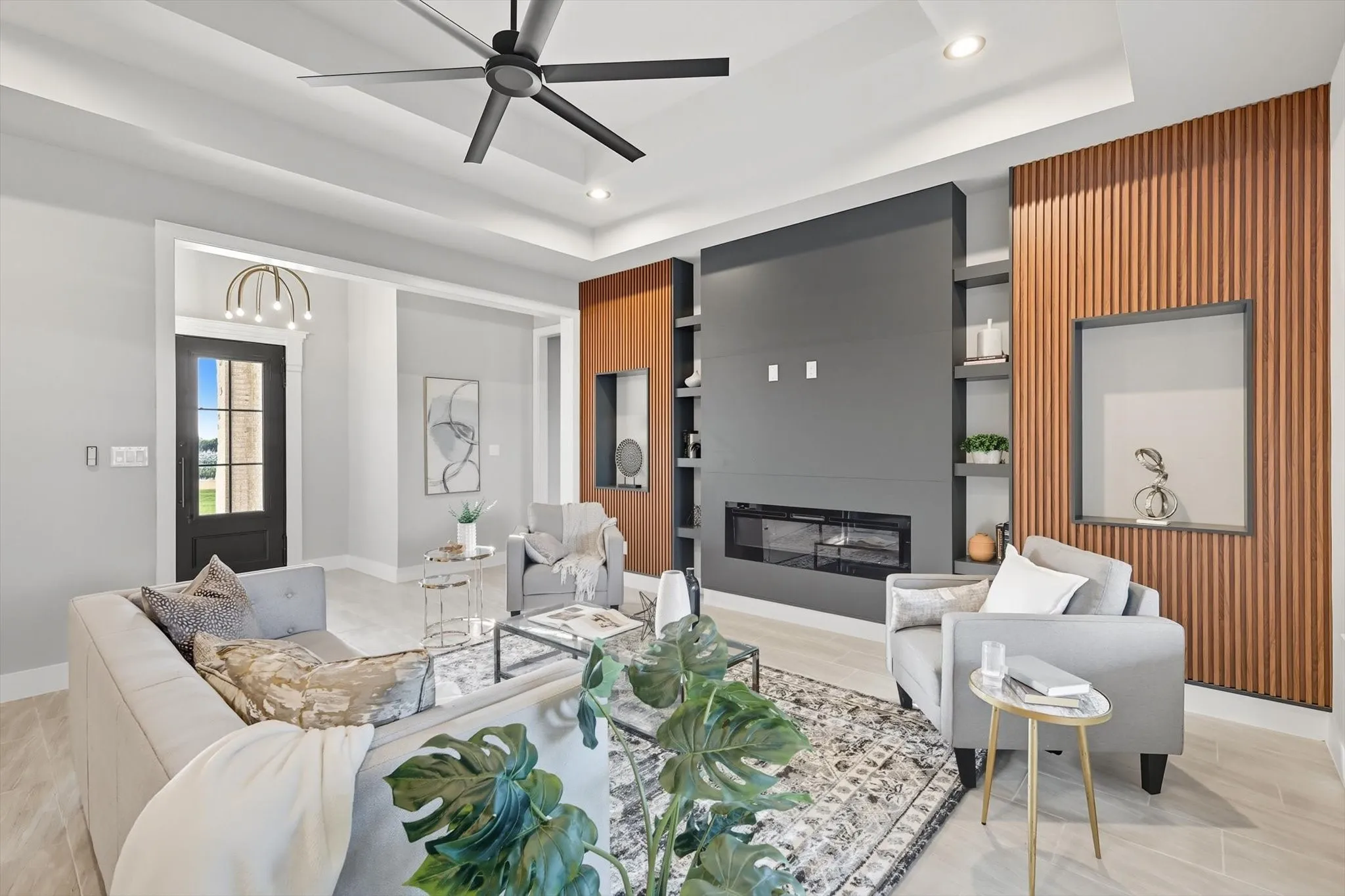Living area featuring built in features, a glass covered fireplace, ceiling fan, a tray ceiling, and recessed lighting