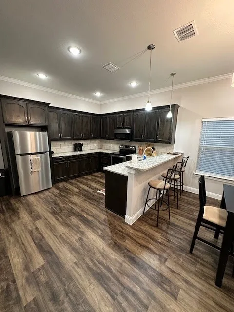 Kitchen with backsplash, a peninsula, refrigerator, crown molding, and stainless steel electric range oven