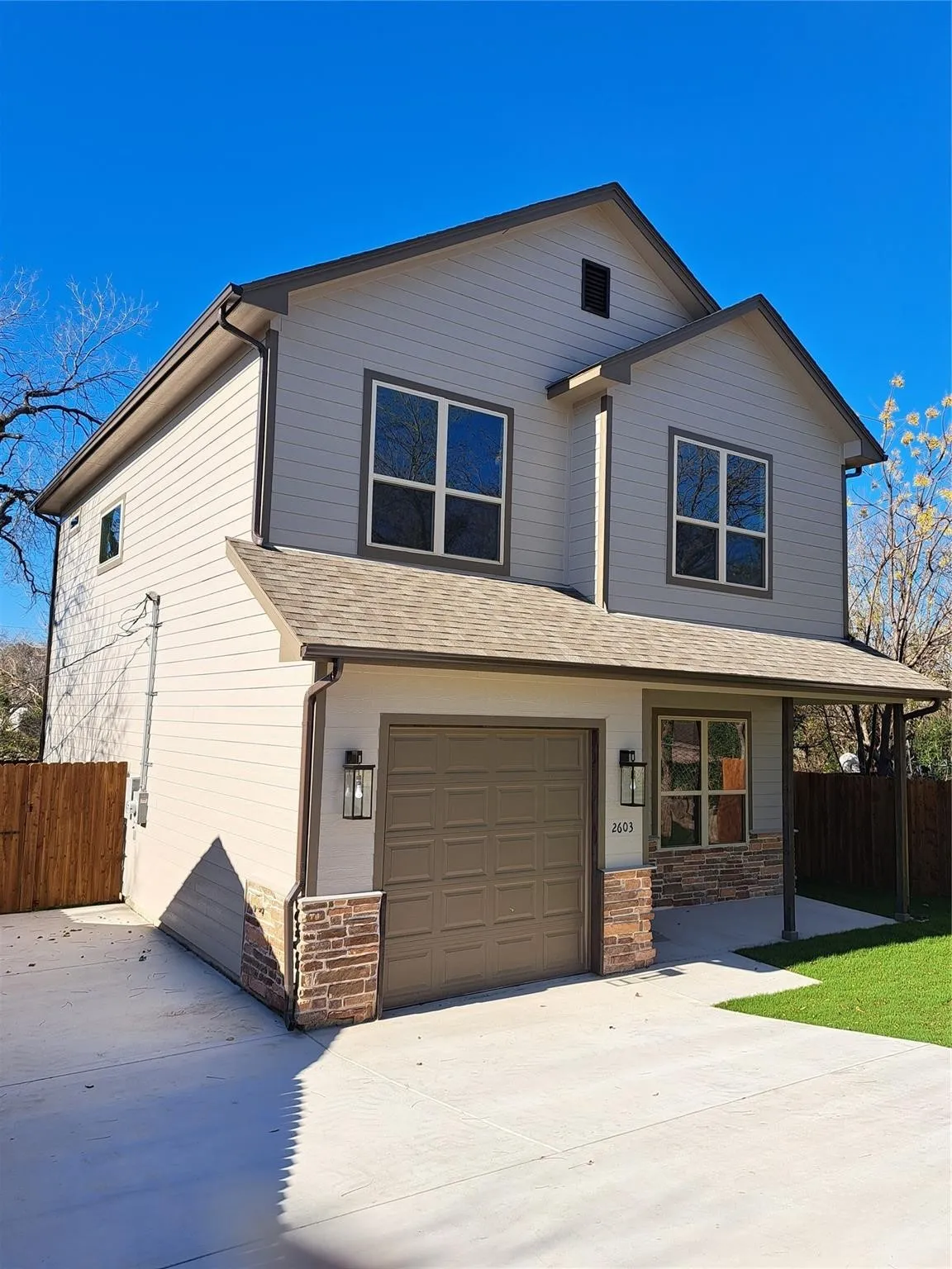 Traditional-style house with a shingled roof, an attached garage, covered porch, driveway, and stone siding