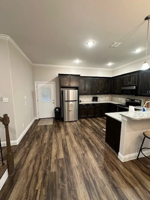 Kitchen with ornamental molding, a kitchen bar, freestanding refrigerator, stove, and backsplash