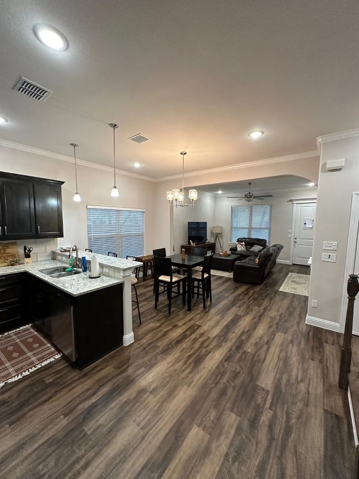 Kitchen with hanging light fixtures, crown molding, open floor plan, dark cabinets, and light stone counters