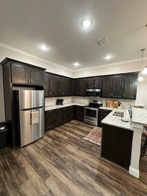 Kitchen with crown molding, refrigerator, stove, decorative light fixtures, and black microwave