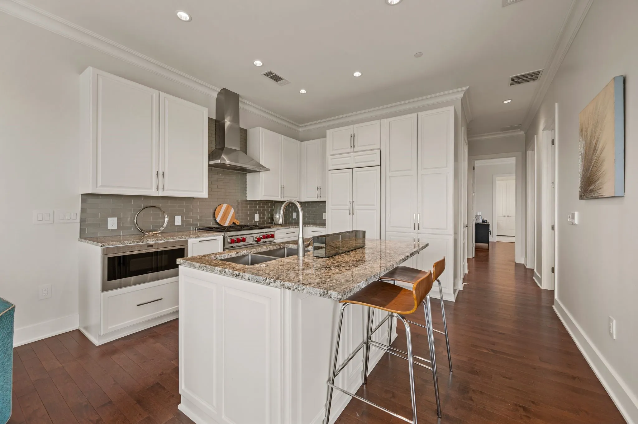 Kitchen featuring white cabinetry, backsplash, ornamental molding, light stone countertops, and wall chimney range hood