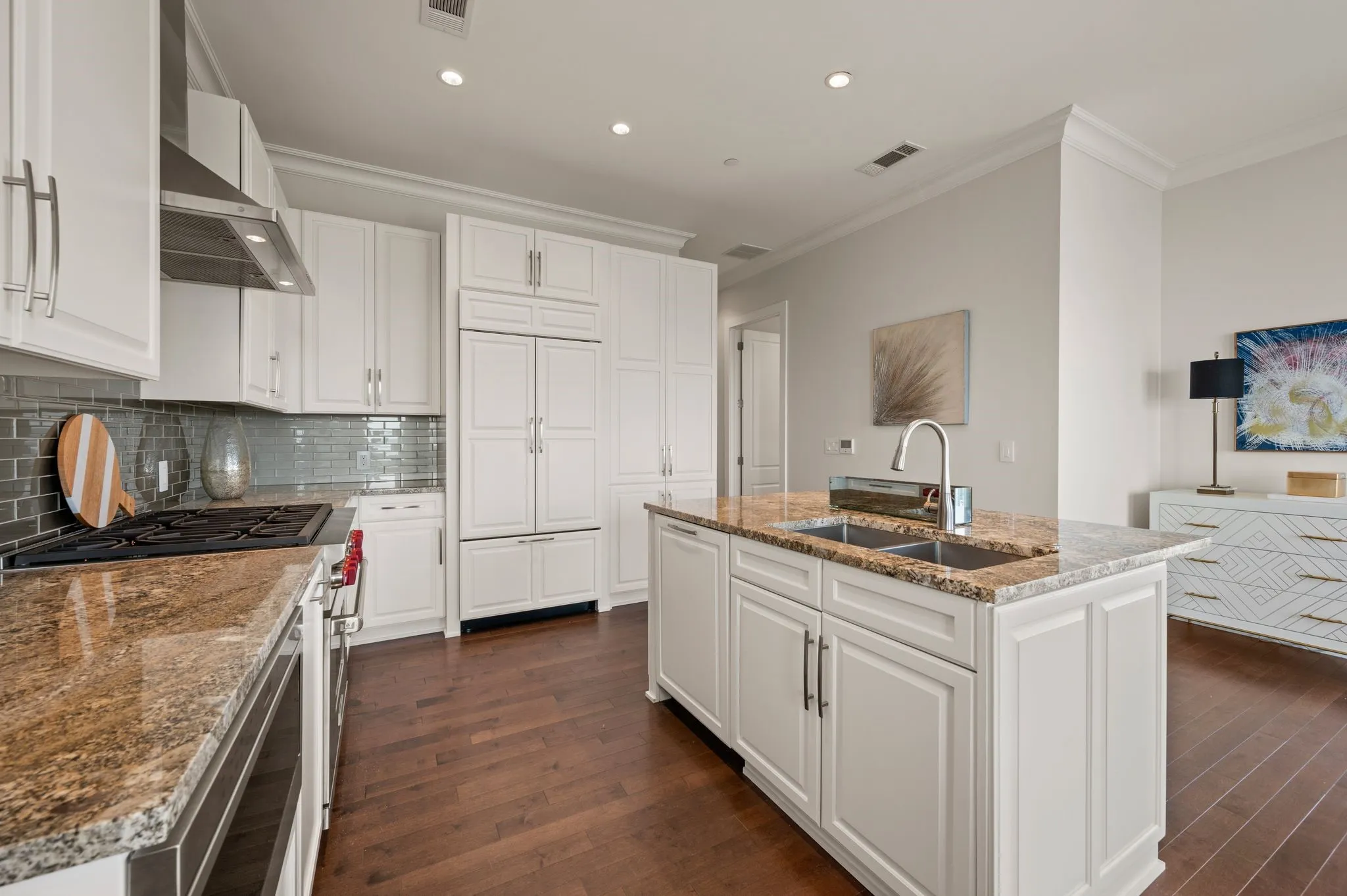 Kitchen with white cabinets, light stone countertops, a kitchen island with sink, stainless steel range with gas stovetop, and wall chimney exhaust hood