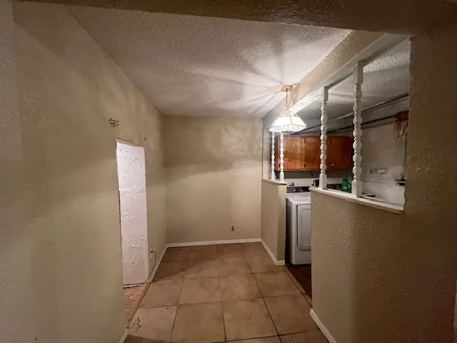 Laundry room featuring a textured wall, light tile patterned floors, a textured ceiling, cabinet space, and washer / dryer