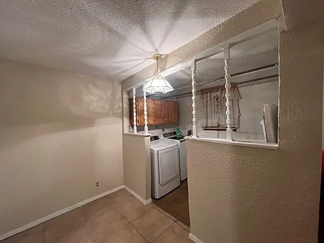 Washroom with a textured wall, tile patterned floors, a textured ceiling, cabinet space, and washer and clothes dryer