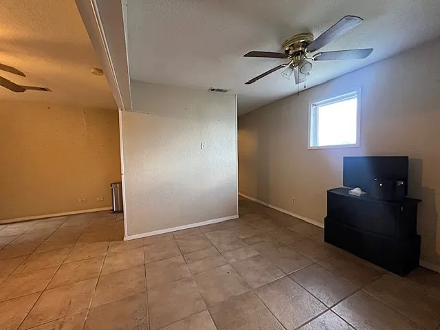 Empty room featuring ceiling fan, a textured ceiling, and light tile patterned floors