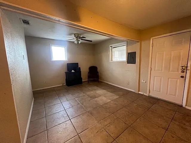 Tiled spare room with a textured wall, ceiling fan, and electric panel