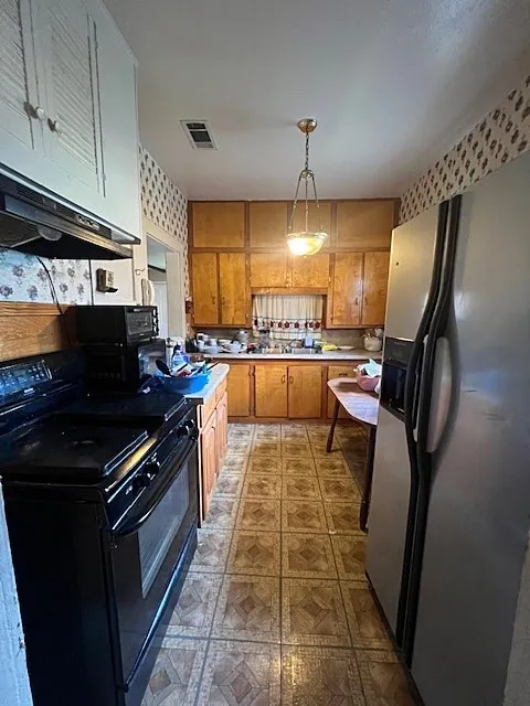 Kitchen featuring stainless steel fridge with ice dispenser, black stove, light countertops, brown cabinetry, and dark floors