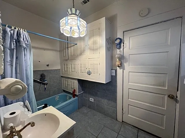 Full bath with shower / tub combo with curtain, dark tile patterned floors, and tile walls