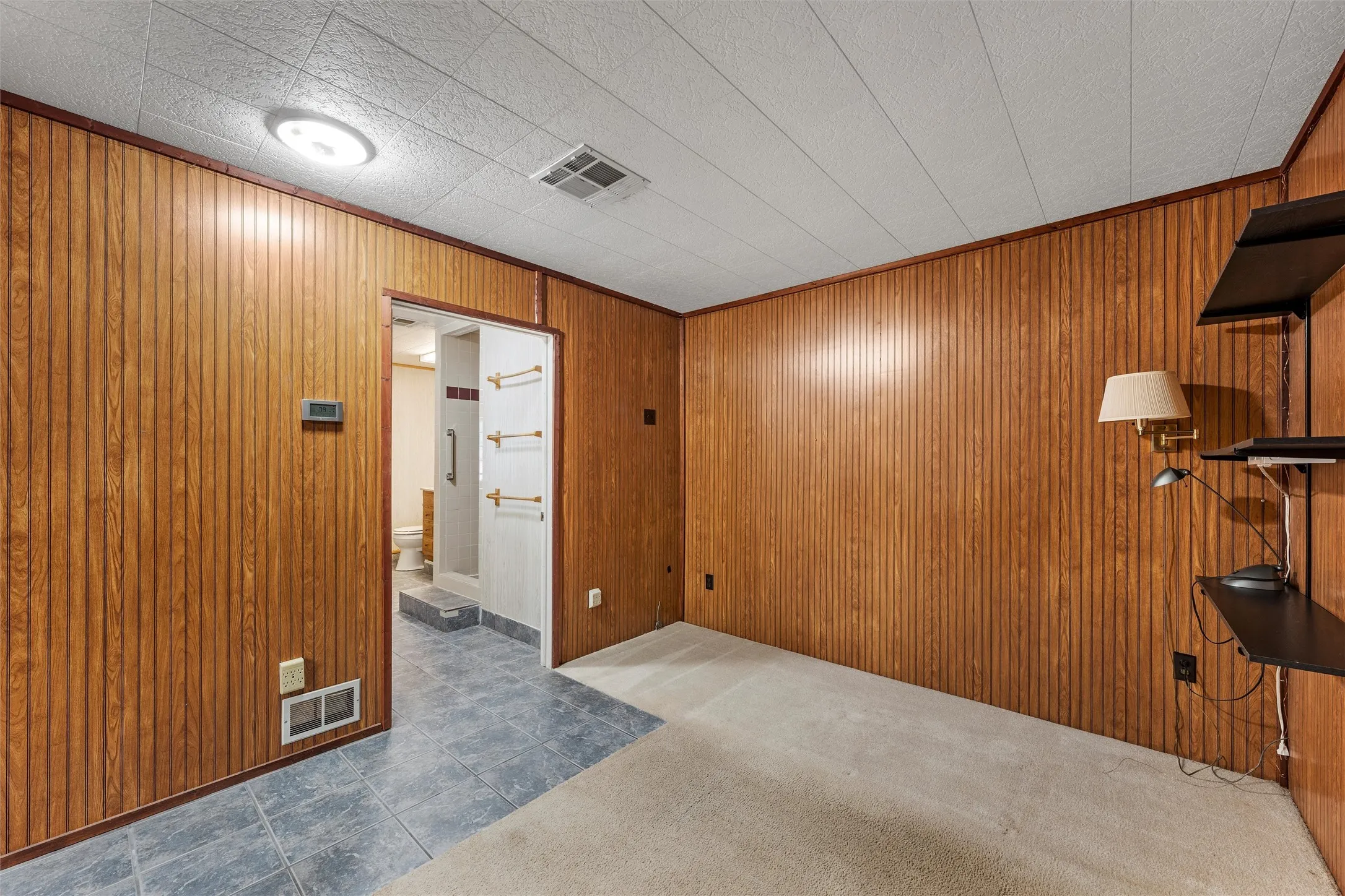 Unfurnished room with wooden walls, dark colored carpet, crown molding, and dark tile patterned floors