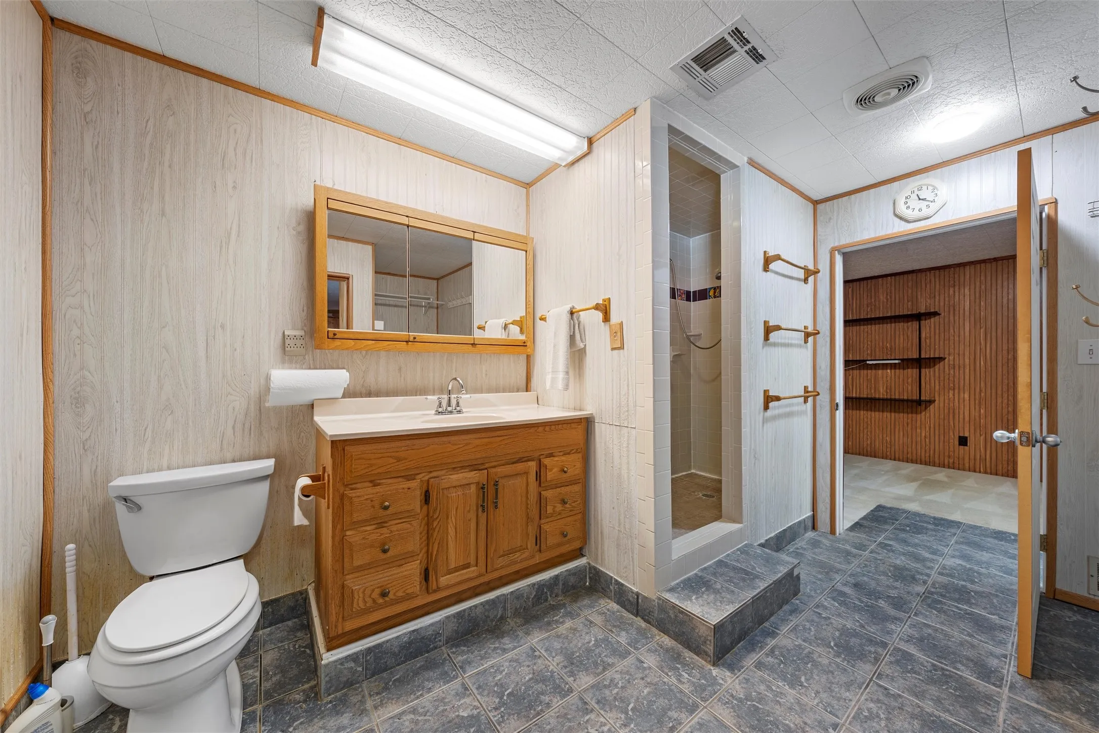 Full bath with a shower stall, vanity, wooden walls, and crown molding