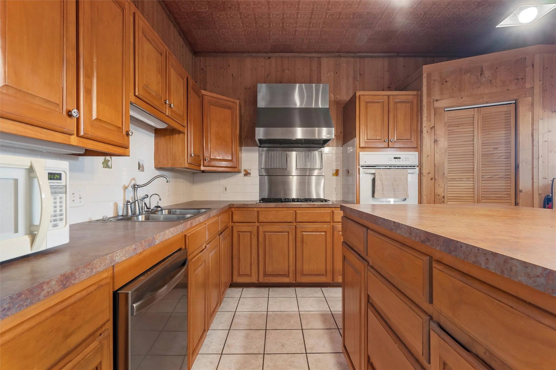 Kitchen with an ornate ceiling, decorative backsplash, brown cabinetry, white appliances, and light tile patterned floors