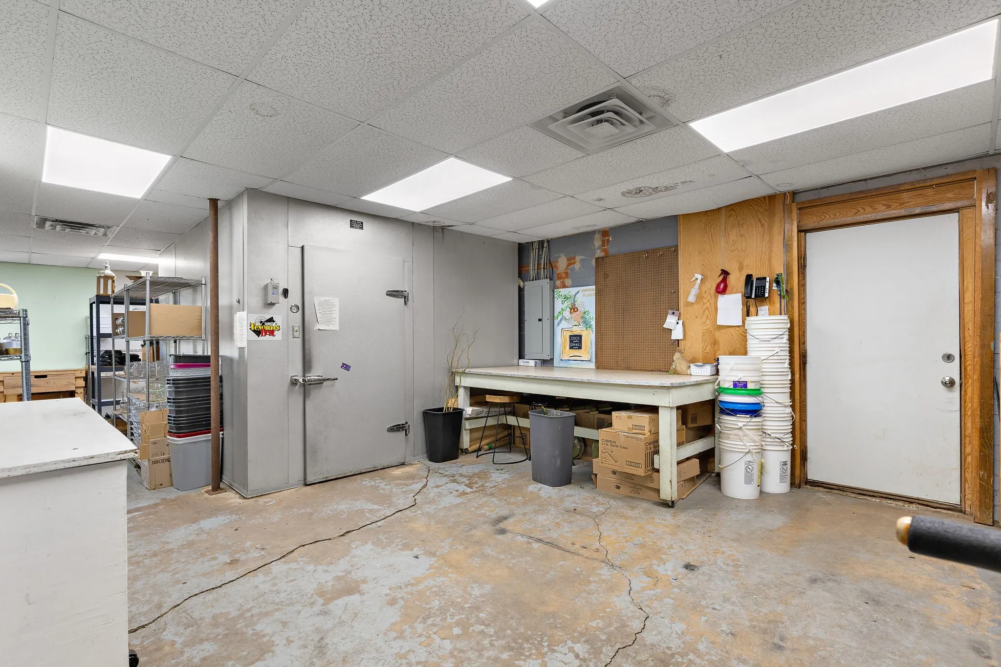 Miscellaneous room featuring a workshop area, a paneled ceiling, unfinished concrete flooring, and electric panel