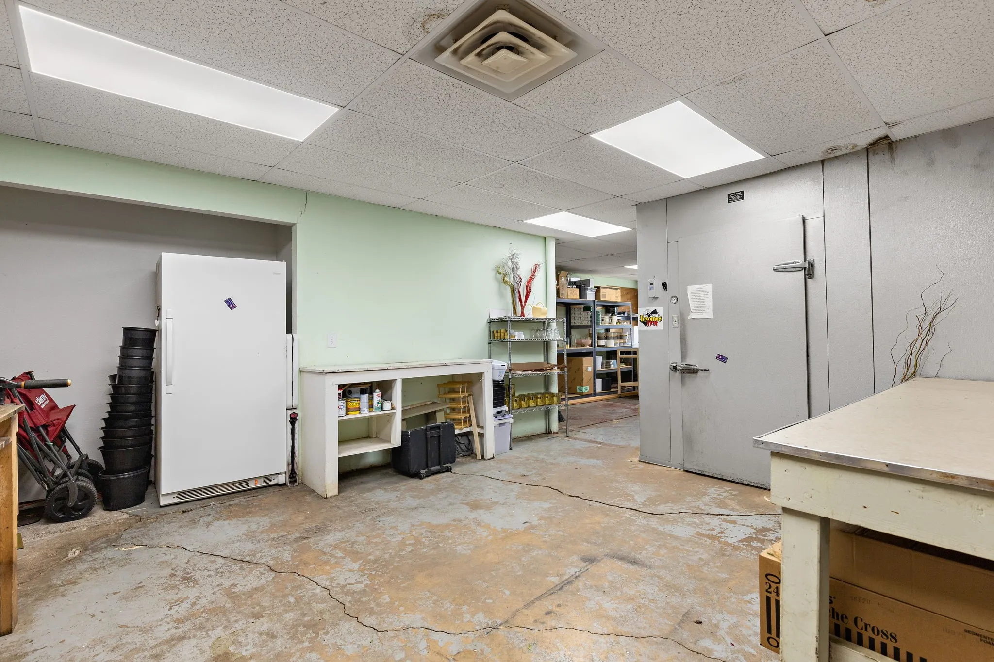 Below grade area featuring freestanding refrigerator, a drop ceiling, and a workshop area