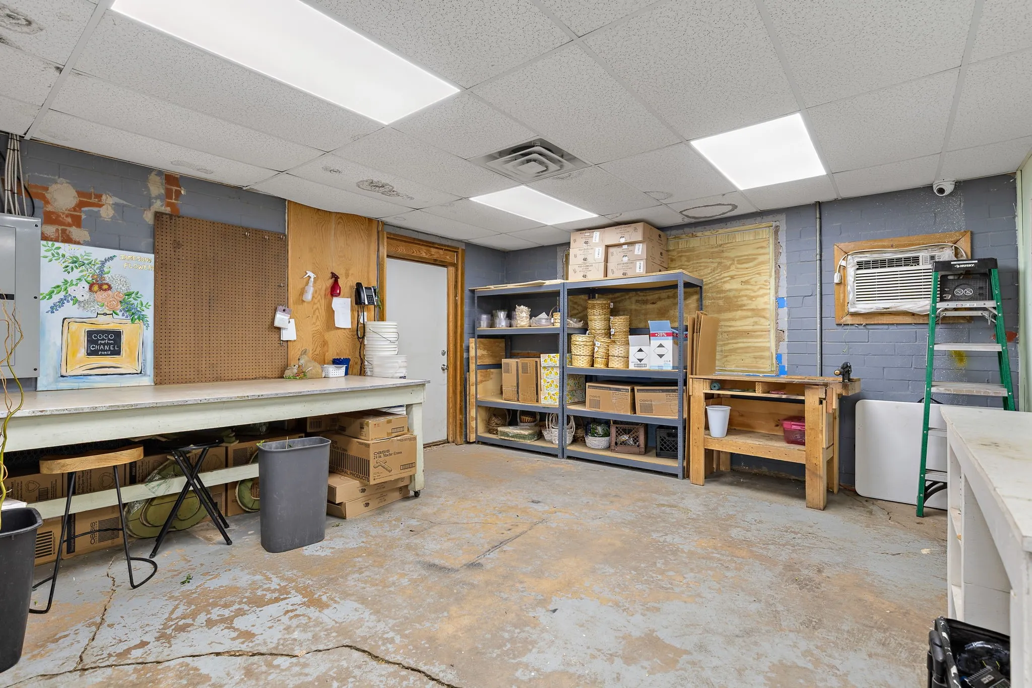 Basement featuring a workshop area, a paneled ceiling, concrete block wall, electric panel, and an AC wall unit