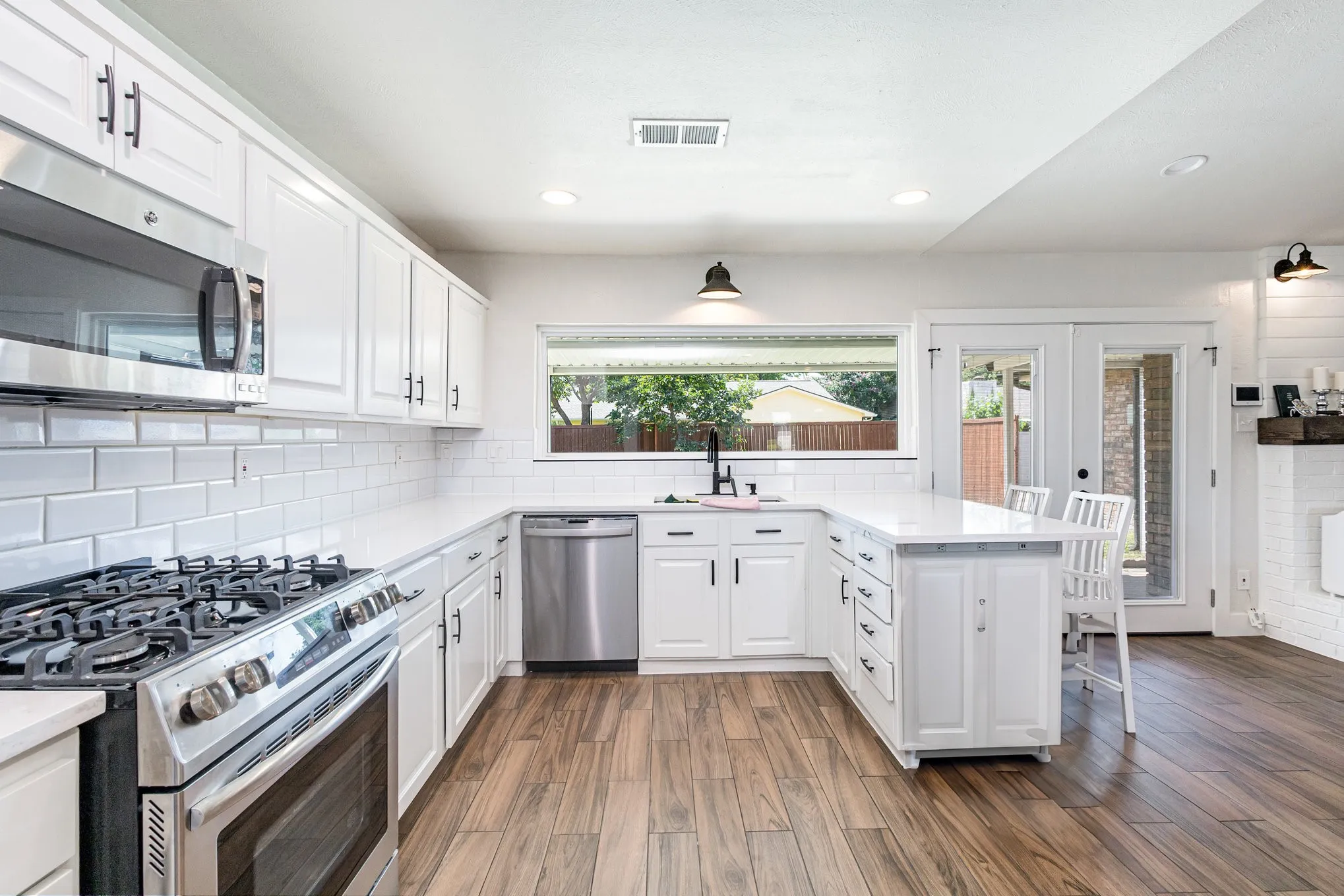 Kitchen with appliances with stainless steel finishes, a peninsula, white cabinets, recessed lighting, and tasteful backsplash