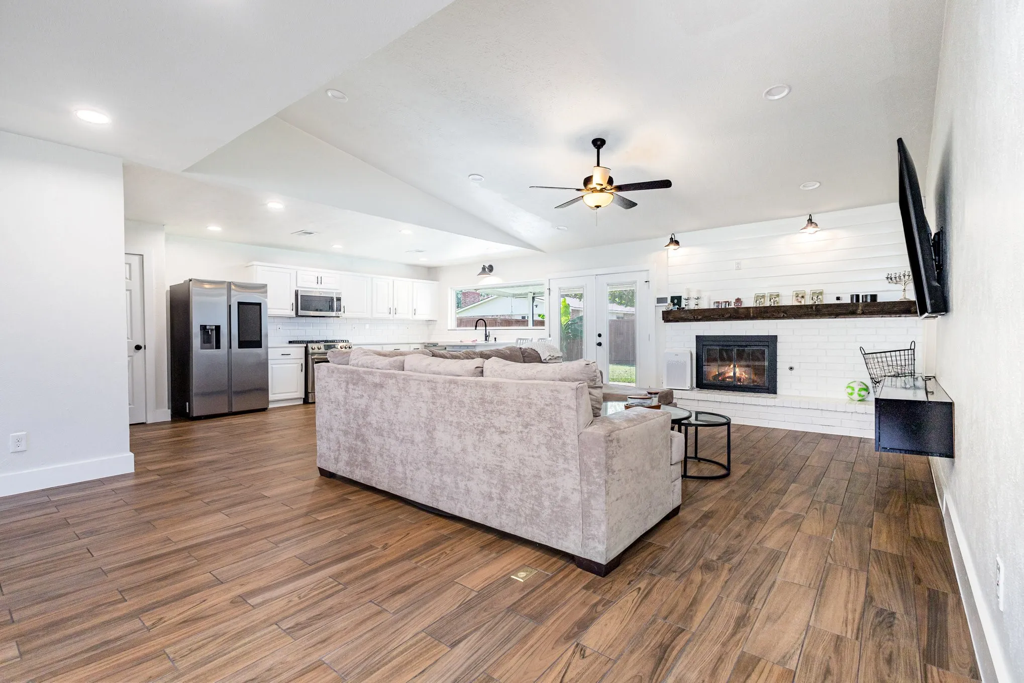Living area featuring vaulted ceiling, dark wood-style floors, recessed lighting, a brick fireplace, and french doors