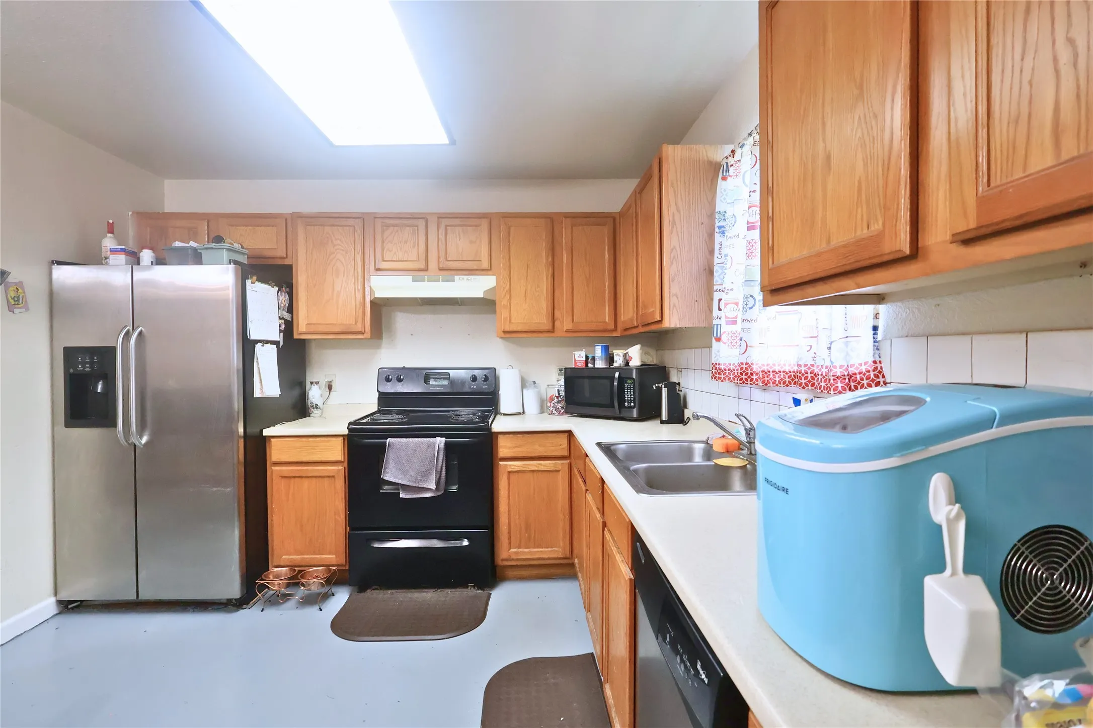 Kitchen featuring black appliances, light countertops, under cabinet range hood, concrete floors, and brown cabinets
