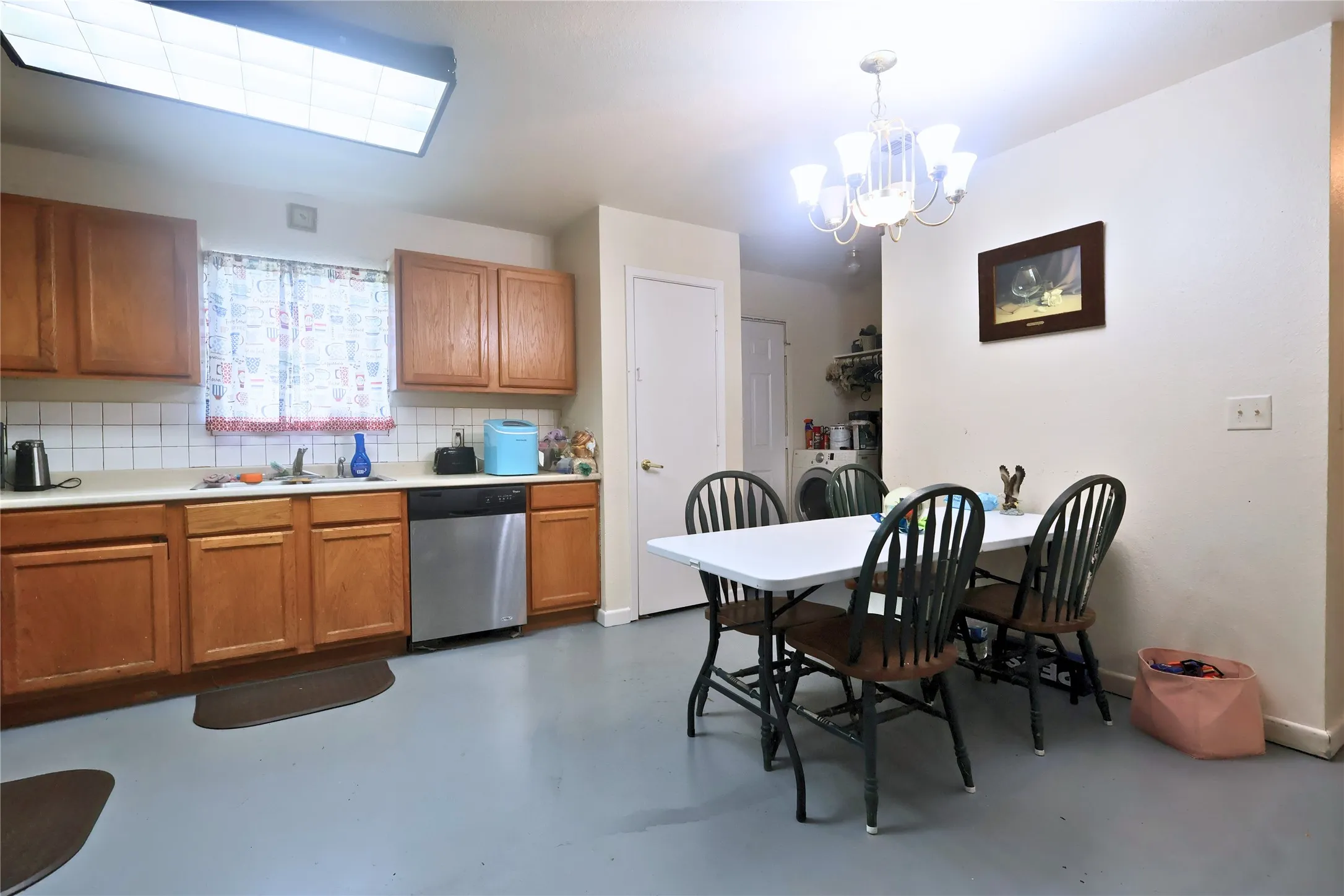 Kitchen with brown cabinets, decorative backsplash, concrete floors, light countertops, and dishwasher