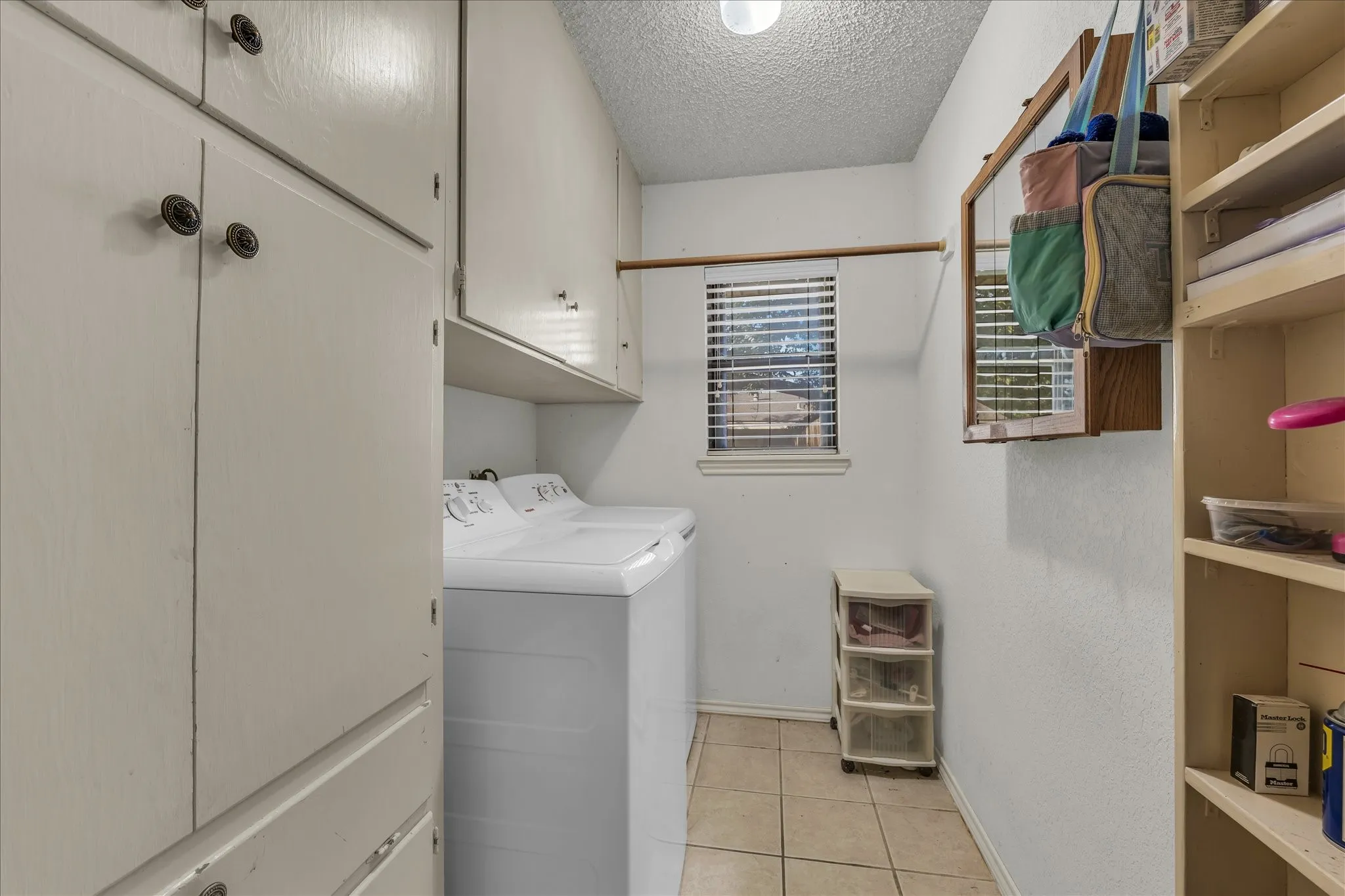 Washroom with light tile patterned floors, a textured ceiling, washing machine and clothes dryer, and cabinet space