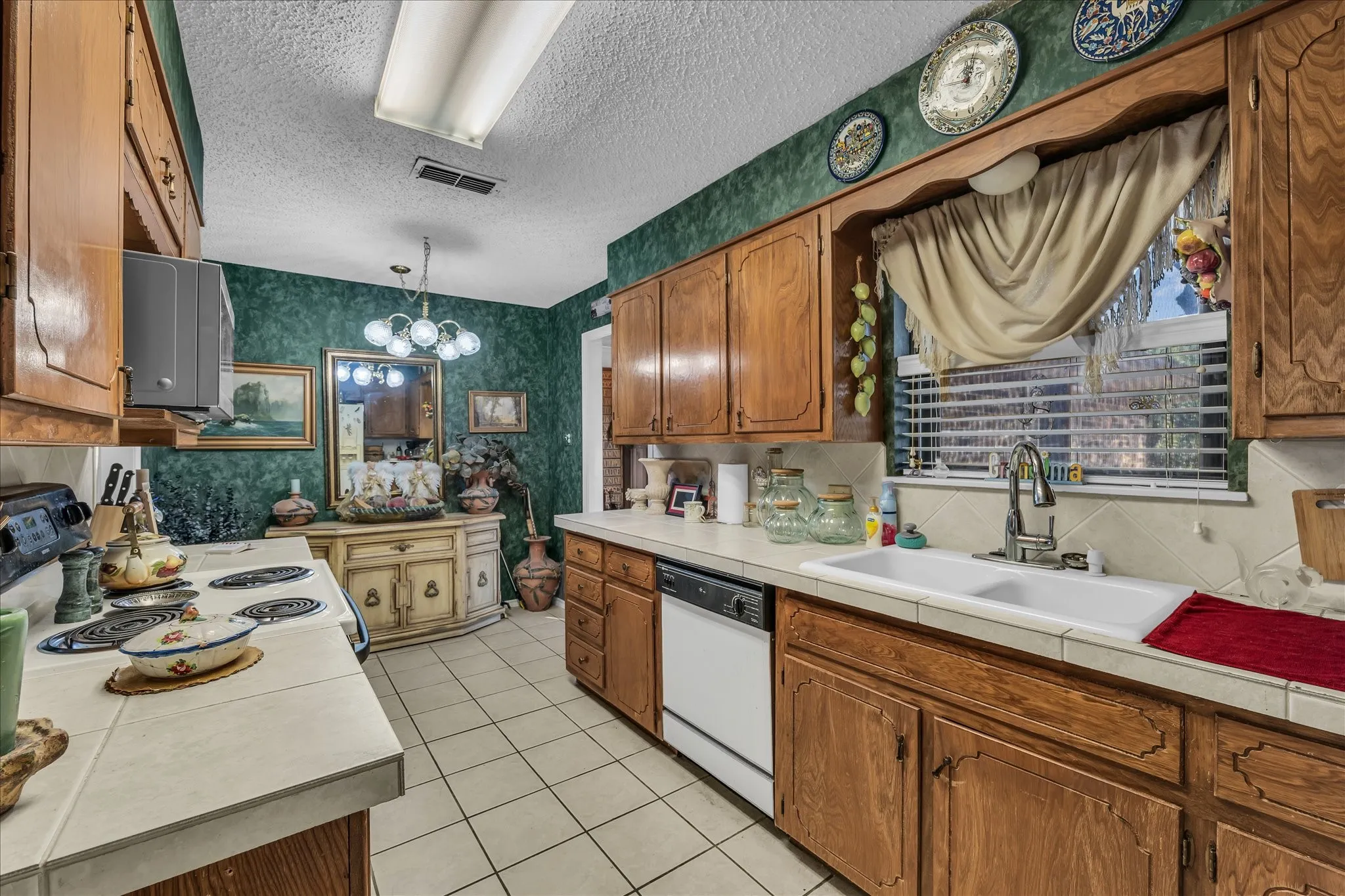 Kitchen featuring wallpapered walls, brown cabinetry, tile countertops, pendant lighting, and white appliances