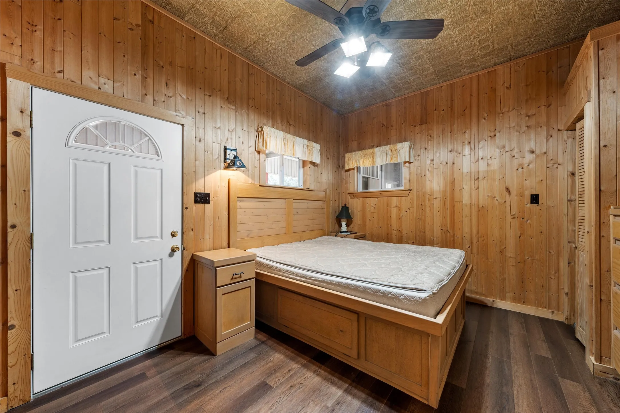 Bedroom with an ornate ceiling, dark wood finished floors, wood walls, and a ceiling fan