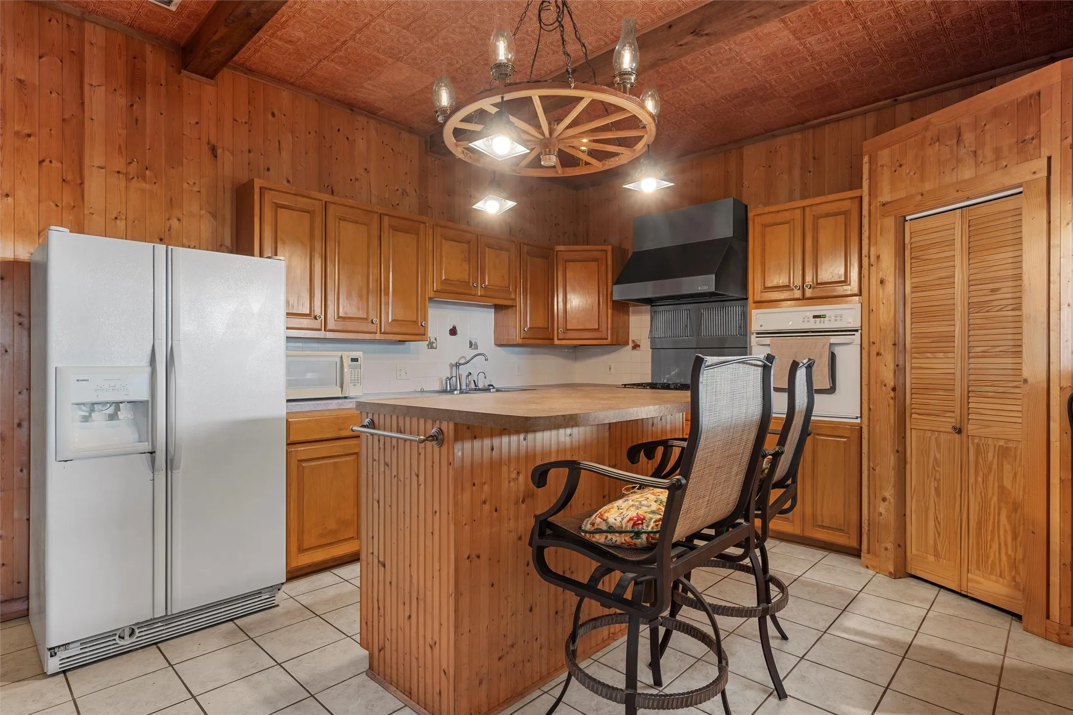 Kitchen with wooden walls, an ornate ceiling, white appliances, light tile patterned floors, and pendant lighting