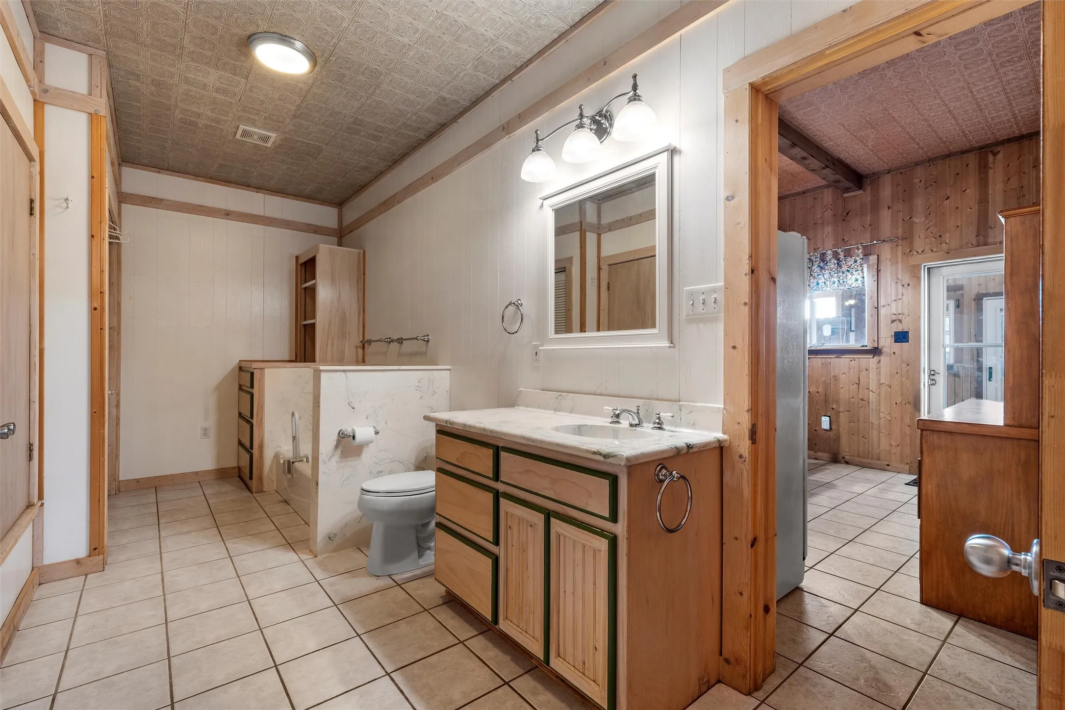 Bathroom with vanity, light tile patterned flooring, wooden walls, and an ornate ceiling