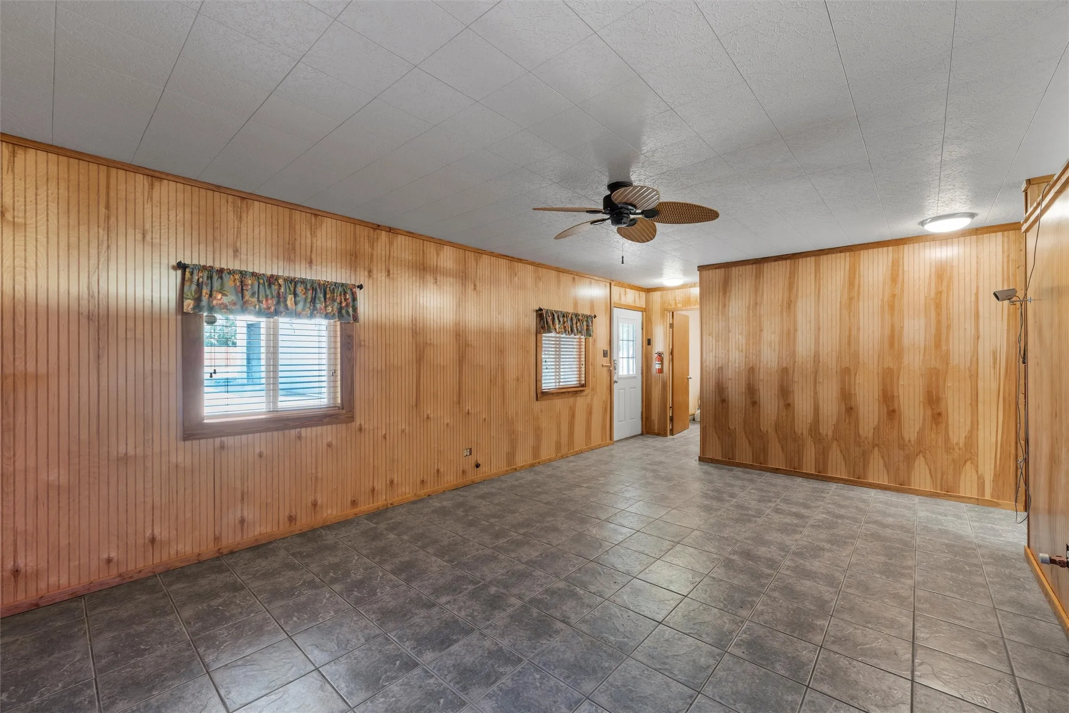 Unfurnished living room with ceiling fan, wooden walls, and ornamental molding