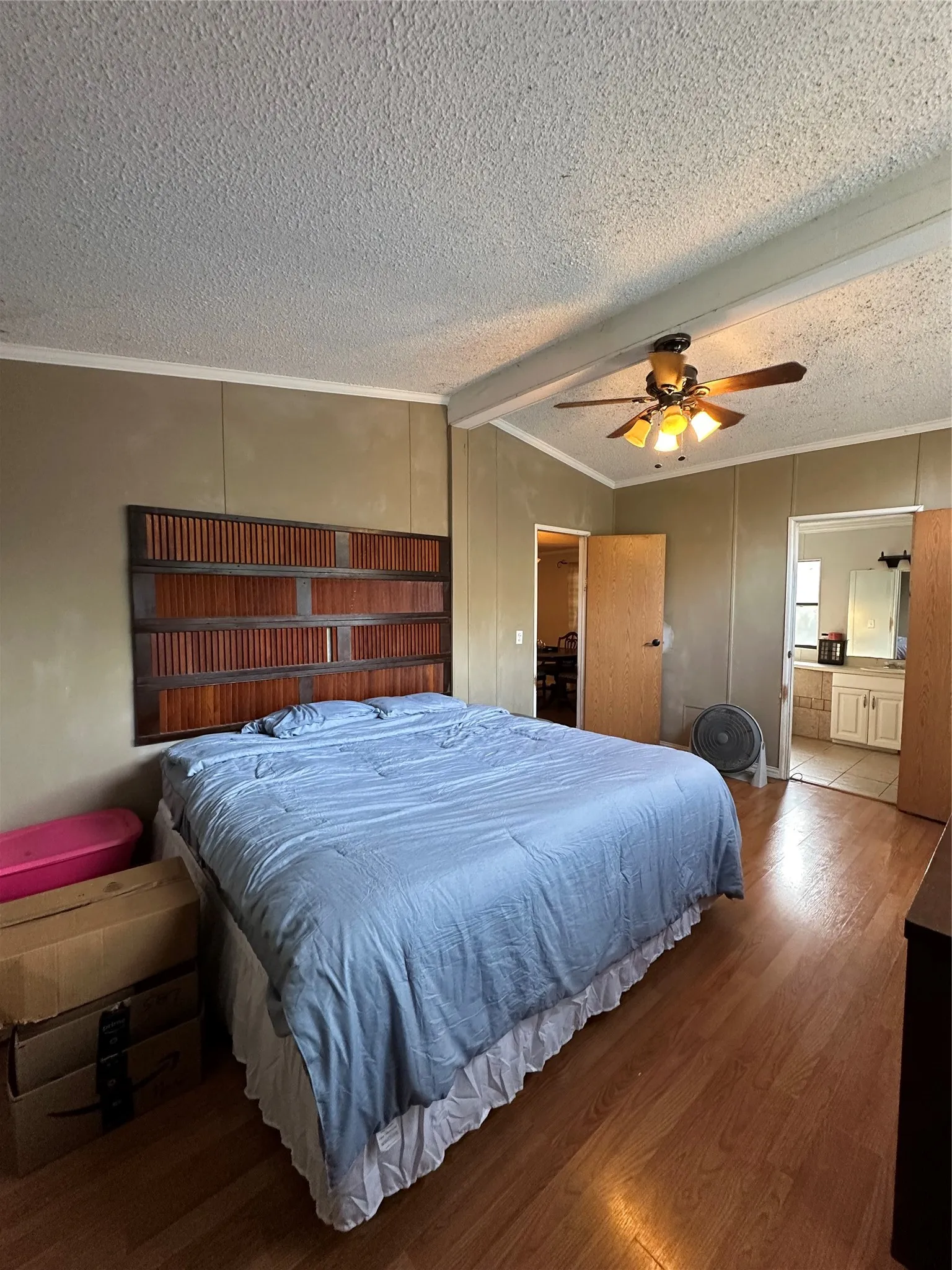 Bedroom with crown molding, wood finished floors, ensuite bath, a textured ceiling, and a ceiling fan