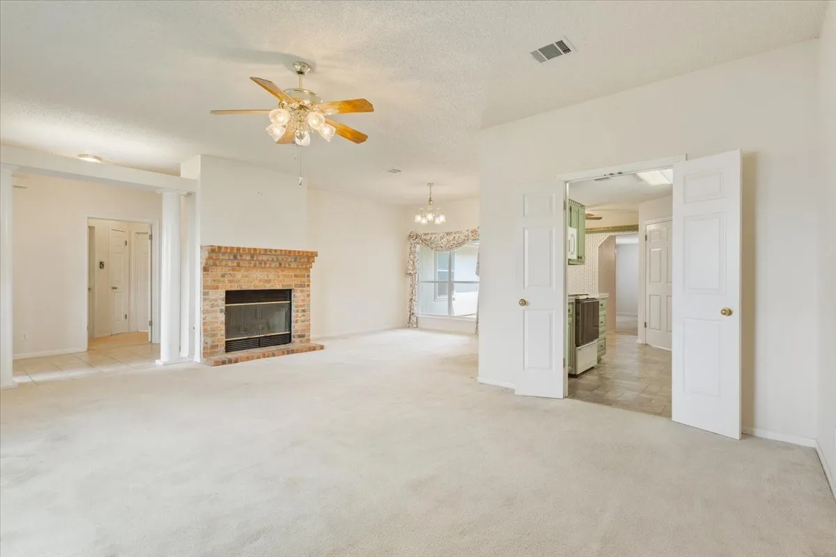 Unfurnished living room with light colored carpet, a textured ceiling, a fireplace, ceiling fan, and a chandelier
